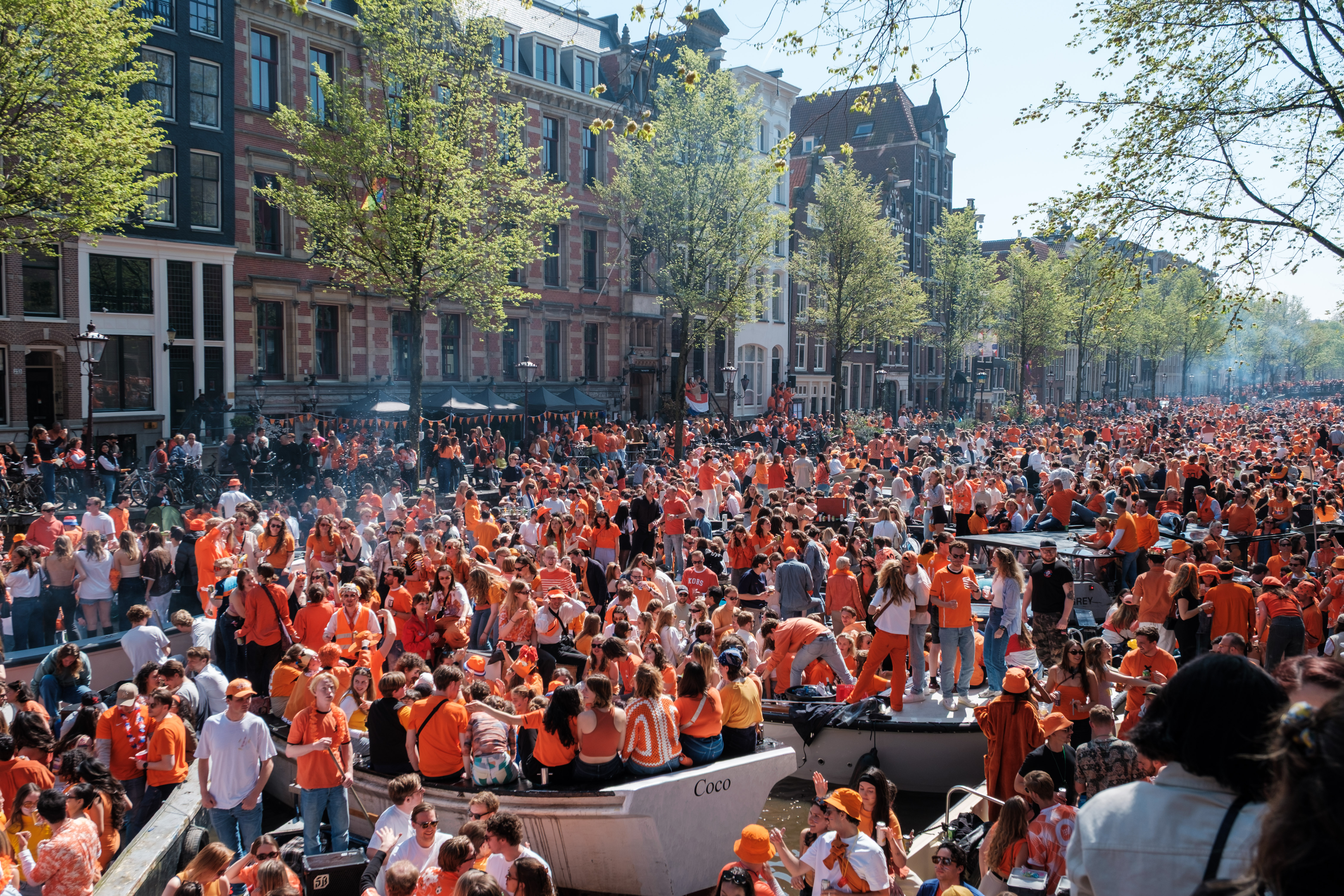 A large crowd celebrating on boats in a canal in Amsterdam, with many wearing orange attire.