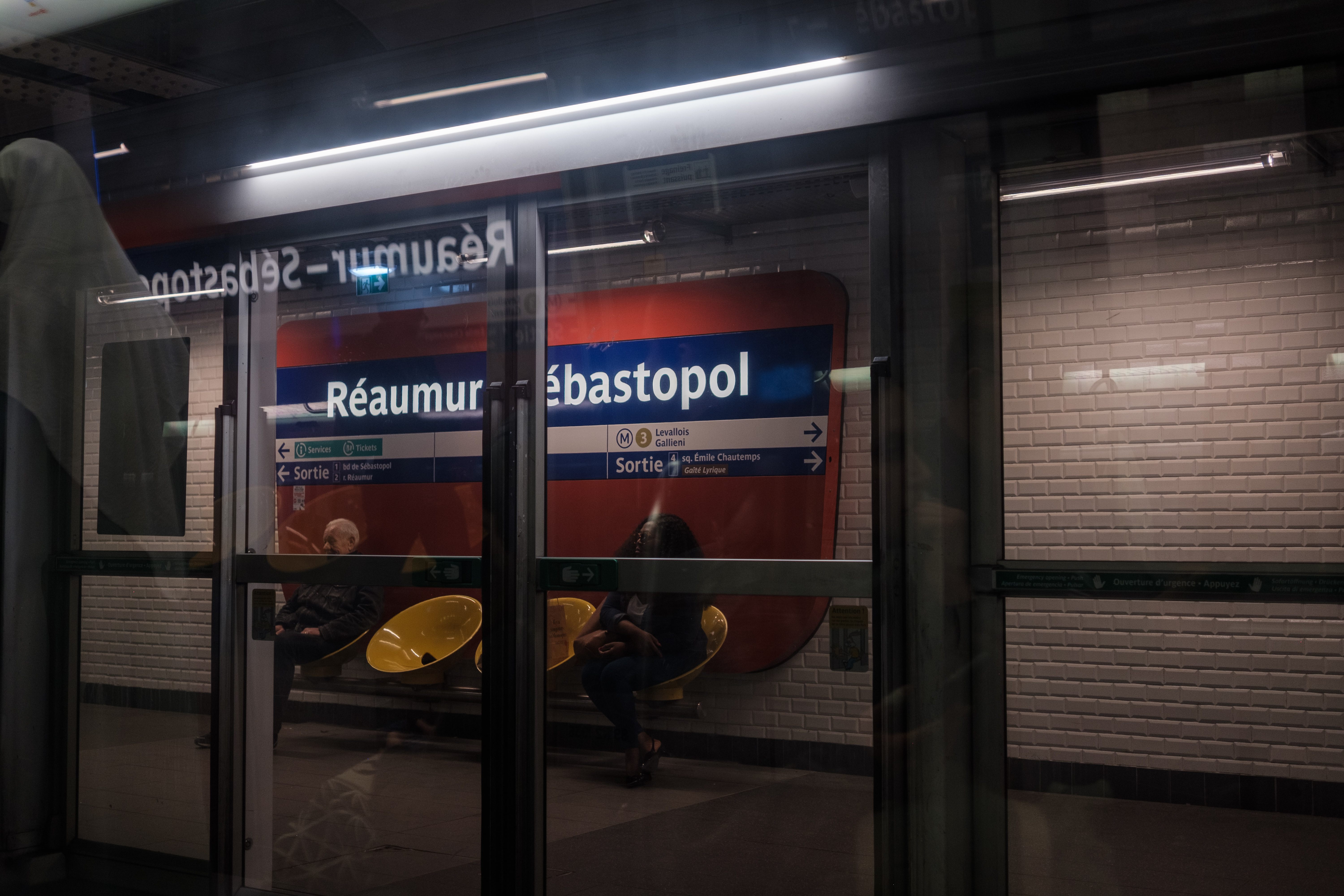 Two people sitting in a metro station named Réaumur-Sébastopol.