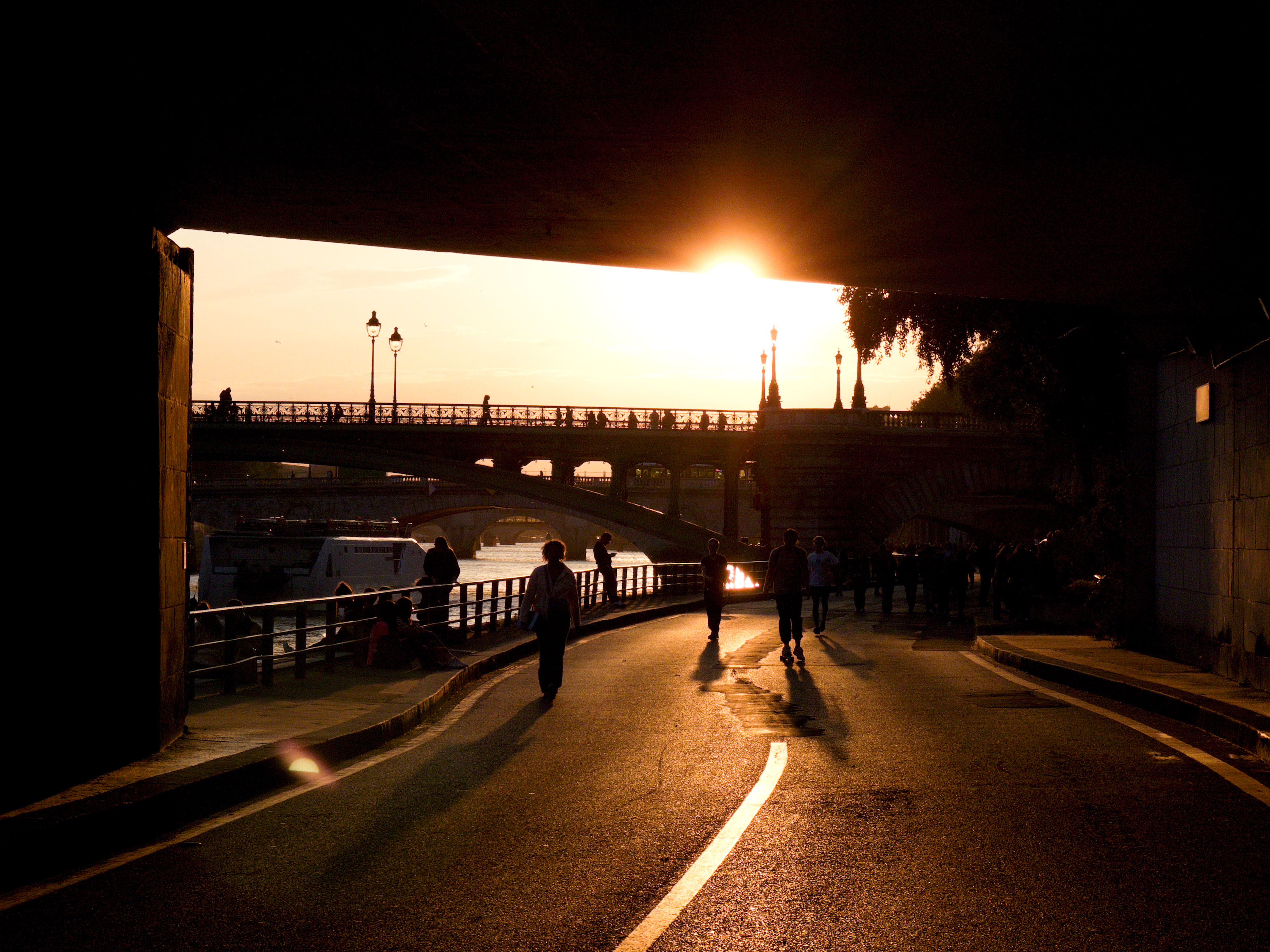 People walking under a bridge with a sunset in the background, Paris.