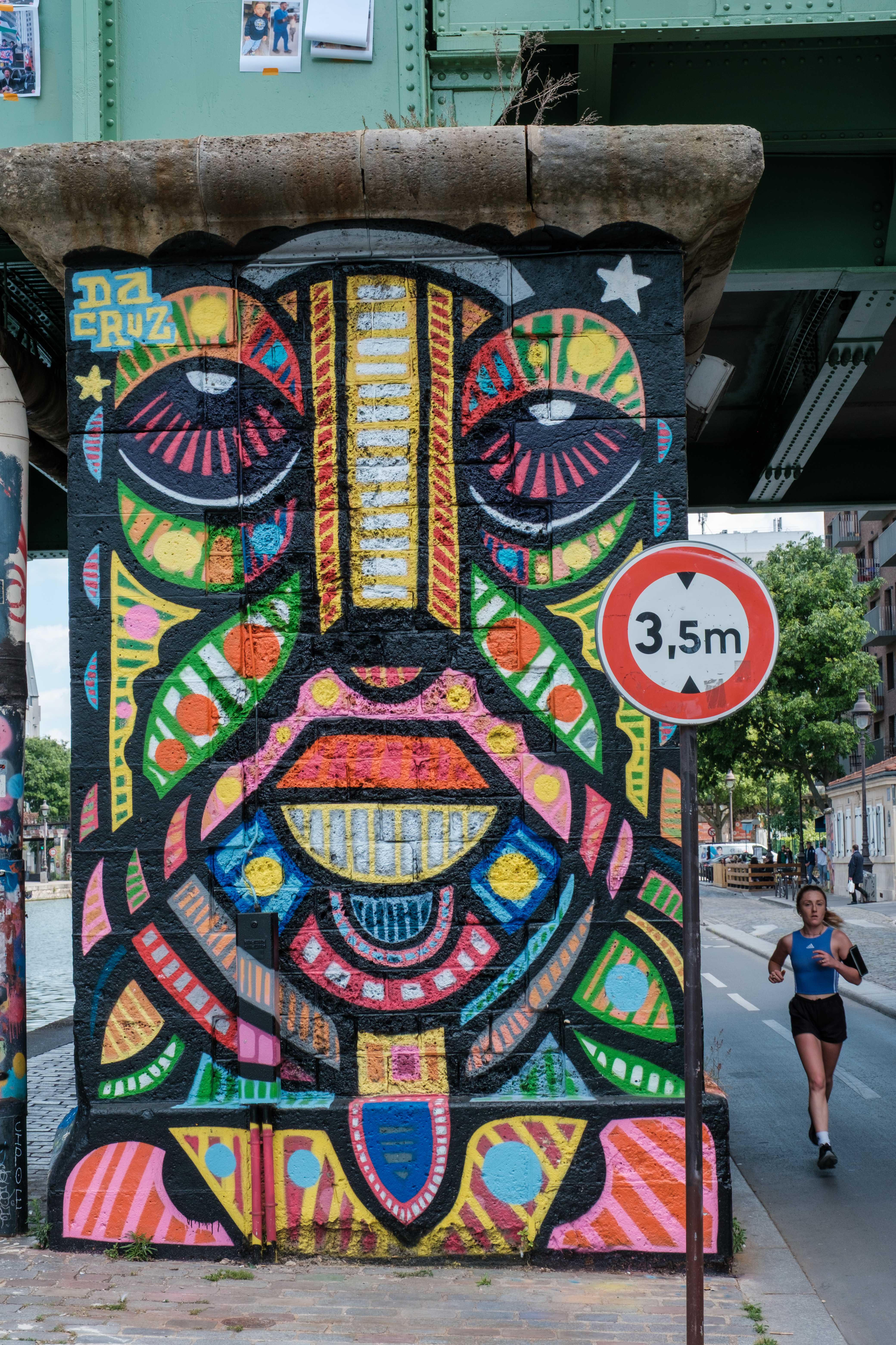 Colorful mural under a bridge with a jogger passing by in Quai de la Loire, Paris.