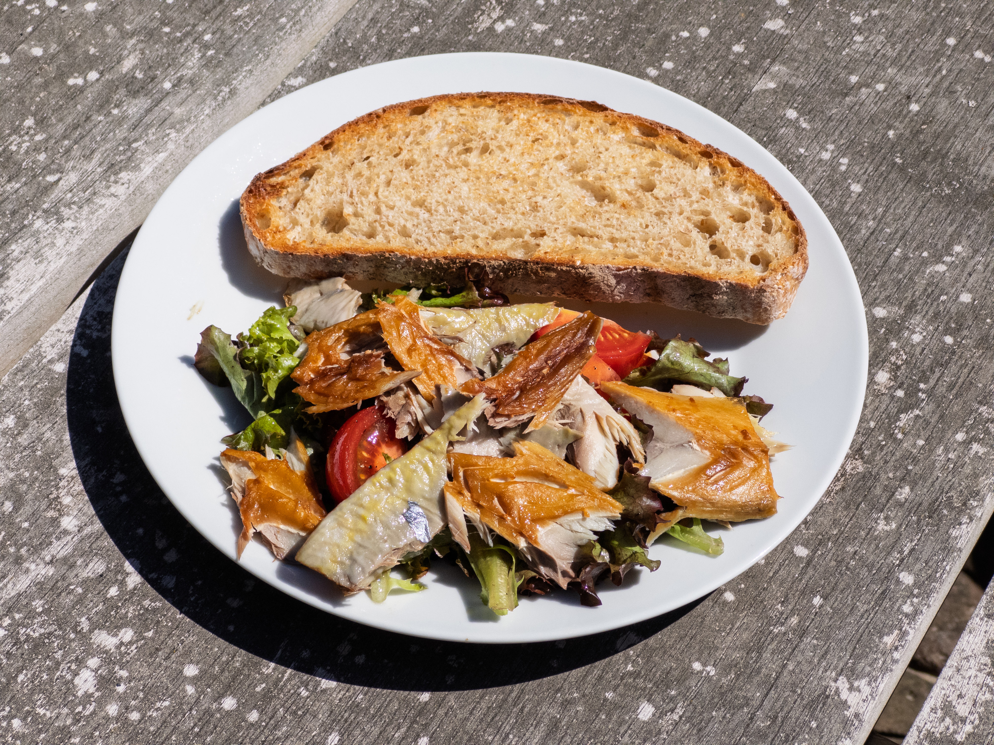 A salad with smoked fish and a slice of bread on a white plate.