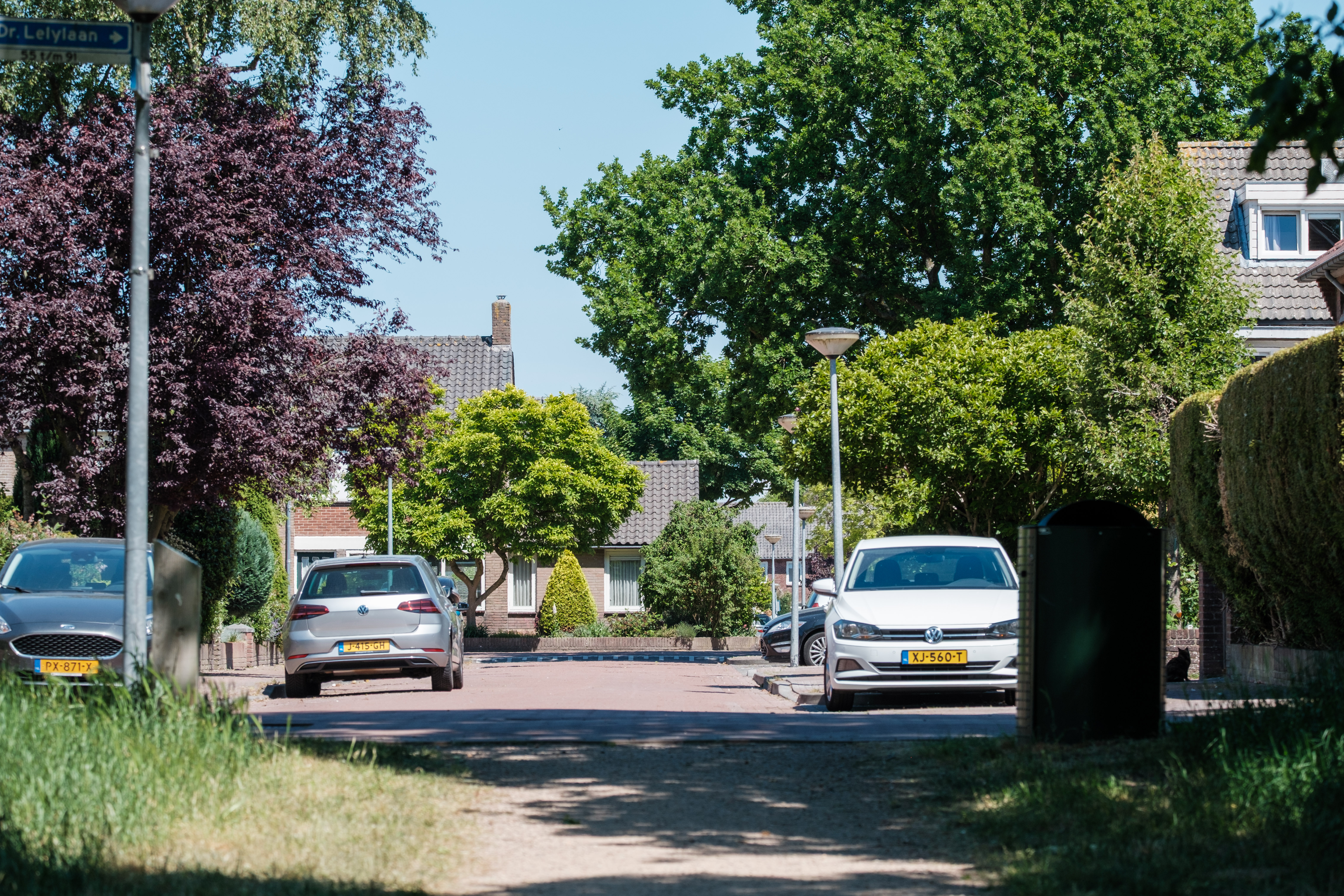 A residential street in Huizen, Netherlands, lined with parked cars and leafy trees.