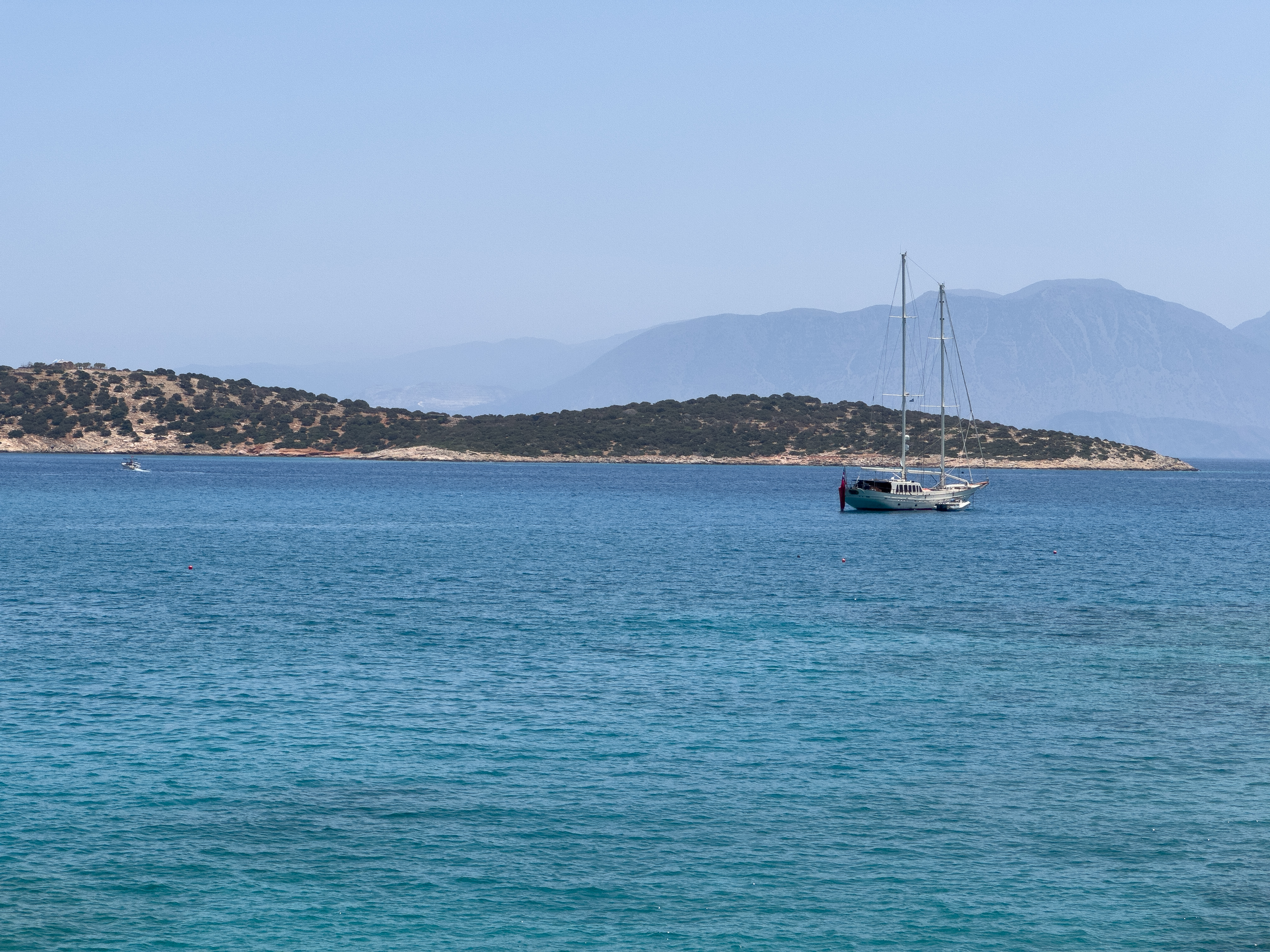 A sailboat anchored near a rocky island in the clear blue sea in Crete.