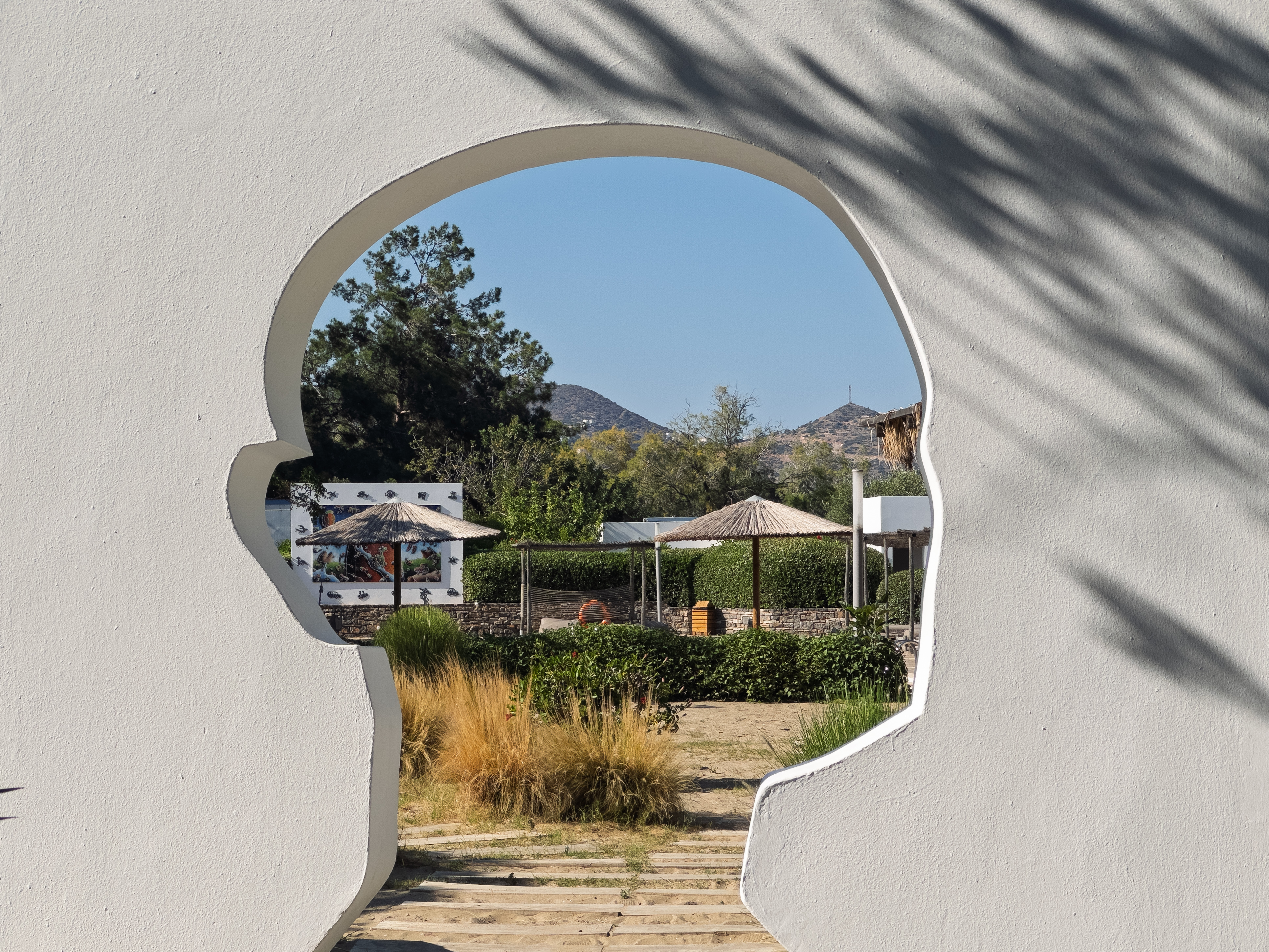 A head-shaped cutout in a wall frames a garden view at Minos Beach Art Hotel in Crete, Greece.