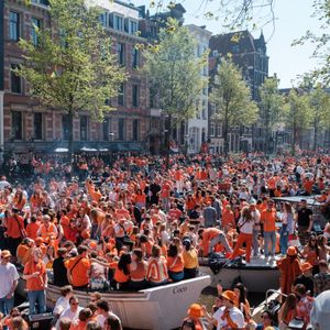 A large crowd celebrating on boats in a canal in Amsterdam, with many wearing orange attire.