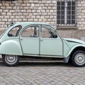 A vintage light green car parked on a stone street in front of a brick wall.