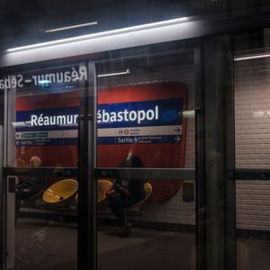Two people sitting in a metro station named Réaumur-Sébastopol.