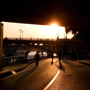People walking under a bridge with a sunset in the background, Paris.