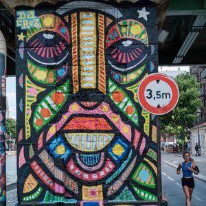 Colorful mural under a bridge with a jogger passing by in Quai de la Loire, Paris.