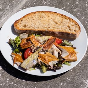 A salad with smoked fish and a slice of bread on a white plate.