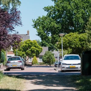 A residential street in Huizen, Netherlands, lined with parked cars and leafy trees.