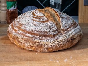 A freshly baked round loaf of crusty bread on a wooden cutting board.