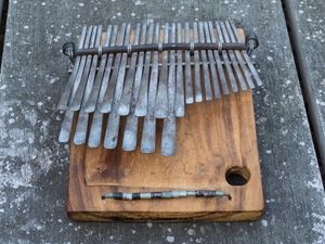 A rustic mbira with metal tines rests on a wooden surface.
